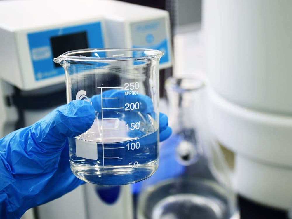 Gloved hand holding a graduated beaker of clear stimulation fluid during lab testing